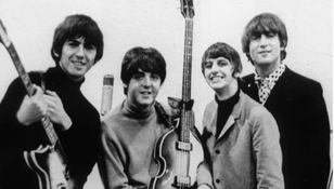 Muzycy z The Beatles z gitarami, uśmiechniętych, pozujących do zdjęcia w czarno-białej tonacji.