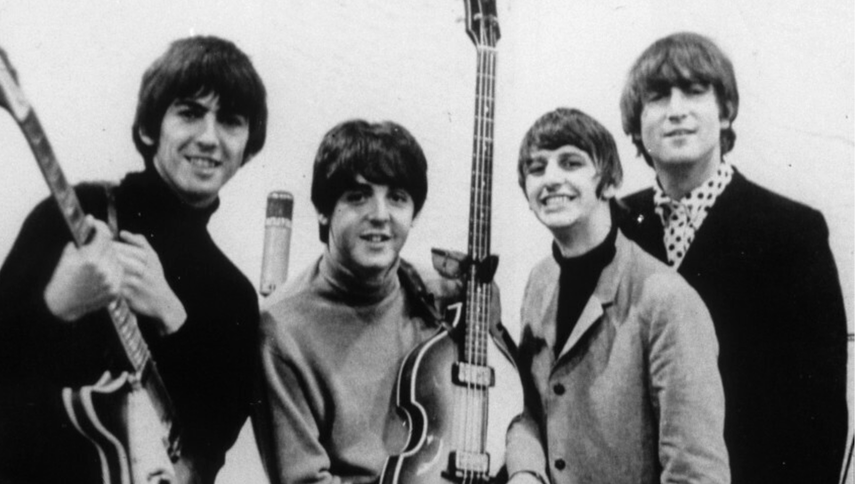 Muzycy z The Beatles z gitarami, uśmiechniętych, pozujących do zdjęcia w czarno-białej tonacji.