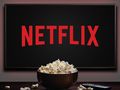 Zdjęcie przedstawia ekran z logo Netflix oraz miskę popcornu na stole.