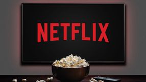 Zdjęcie przedstawia ekran z logo Netflix oraz miskę popcornu na stole.