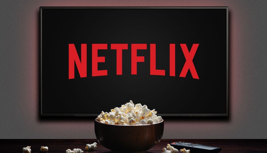 Zdjęcie przedstawia ekran z logo Netflix oraz miskę popcornu na stole.