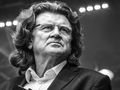 Zbigniew Wodecki. Mężczyzna z długimi włosami, w garniturze, patrzy w stronę widowni, na tle świecących świateł.