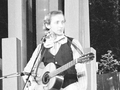 Andrzej Rosiewicz z gitarą na scenie, ubrany w kamizelkę i biały krawat. Czarno-białe zdjęcie.