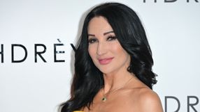 Na zdjęciu uśmiechająca się kobieta z długimi, ciemnymi włosami, w żółtej sukience, na tle logo.