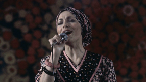 Na zdjęciu widoczna Irena Jarocka śpiewa do mikrofonu, w tle barwny wzór.