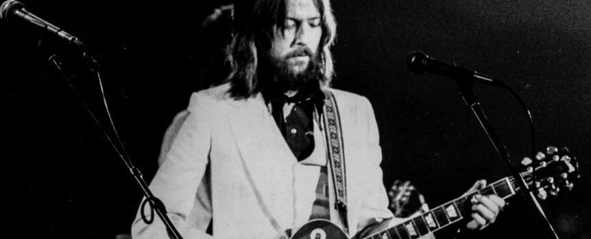 Mężczyzna w jasnym garniturze grający na gitarze elektrycznej na scenie.