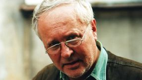 Osoba w okularach, z emocjonalnym wyrazem twarzy, ubrana w brązową kurtkę. Brak informacji o polityku.