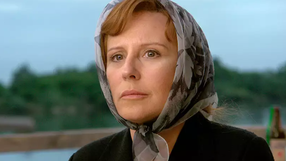 Krystyna Janda - kobieta w chustce z zamyśloną miną, zdjęcie z zielonym krajobrazem w tle.