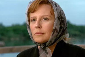 Krystyna Janda - kobieta w chustce z zamyśloną miną, zdjęcie z zielonym krajobrazem w tle.