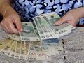 Osoba przelicza banknoty na stół z koronkowym obrusem. Widoczne m.in. banknoty 500 i 100 zł.