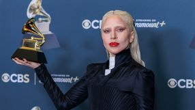 Lady Gaga. Artystka z białymi włosami, trzymająca statuetkę Grammy na tle niebieskiego tła.