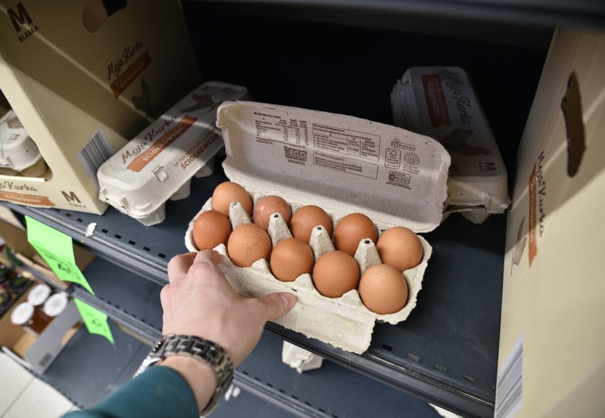 Osoba trzymająca karton z dziesięcioma brązowymi jajkami na półce sklepowej.