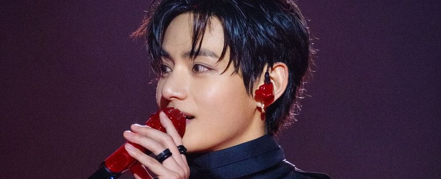 Młody mężczyzna z ciemnymi włosami trzyma czerwony mikrofon, w tle subtelne światła.