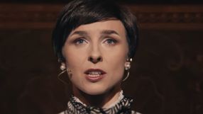 Kobieta z krótkimi włosami, w eleganckiej bluzce, mówi do publiczności na scenie.