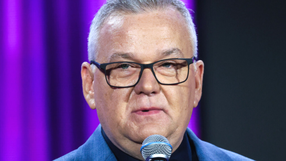 Artur Andrus mówiący do mikrofonu. Tło w kolorze fioletowym.