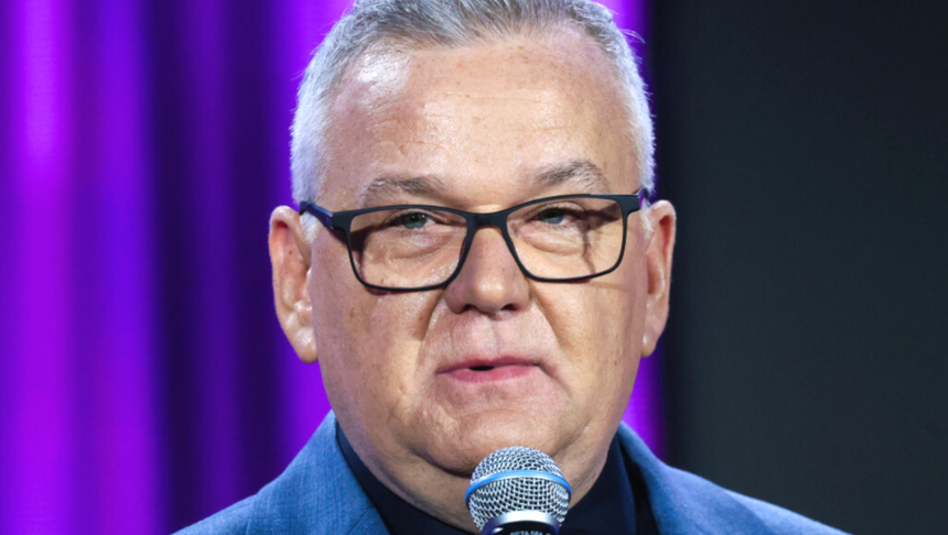 Artur Andrus mówiący do mikrofonu. Tło w kolorze fioletowym.
