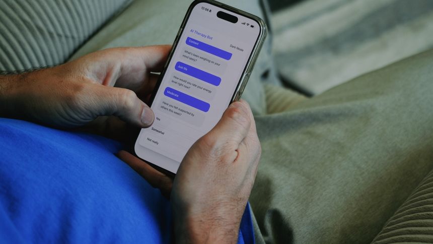 Mężczyzna w granatowej koszulce trzyma telefon, na którym otwarta jest aplikacja do terapii.