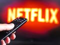 Na zdjęciu widać pilota do telewizora skierowanego na ekran z logo Netflix.