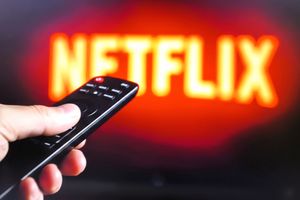 Na zdjęciu widać pilota do telewizora skierowanego na ekran z logo Netflix.