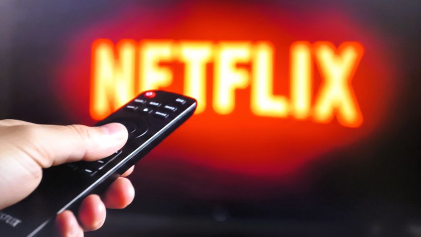 Na zdjęciu widać pilota do telewizora skierowanego na ekran z logo Netflix.
