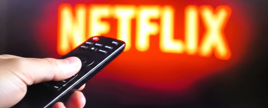 Na zdjęciu widać pilota do telewizora skierowanego na ekran z logo Netflix.