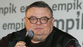 Mężczyzna trzyma mikrofon, ma okrągłe okulary i bladą cerę, siedzi na tle napisu Empik.