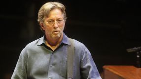 Na zdjęciu mężczyzna z gitarą, w okularach, w niebieskiej koszuli, na scenie.