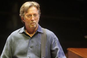 Na zdjęciu mężczyzna z gitarą, w okularach, w niebieskiej koszuli, na scenie.
