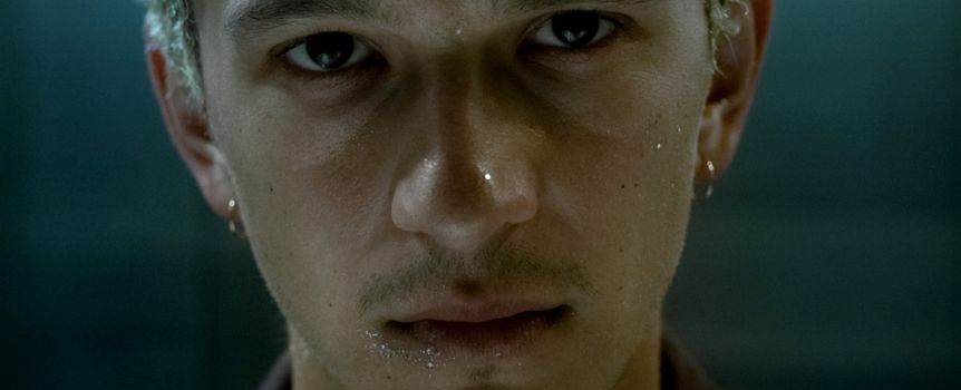 Mężczyzna z krótkimi, jasnymi włosami, intensywnym spojrzeniem i kroplami wody na twarzy.