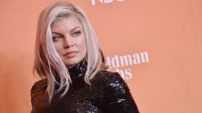 Wizerunek kobiety z długimi, jasnymi włosami w czarnej, błyszczącej sukience na pomarańczowym tle.