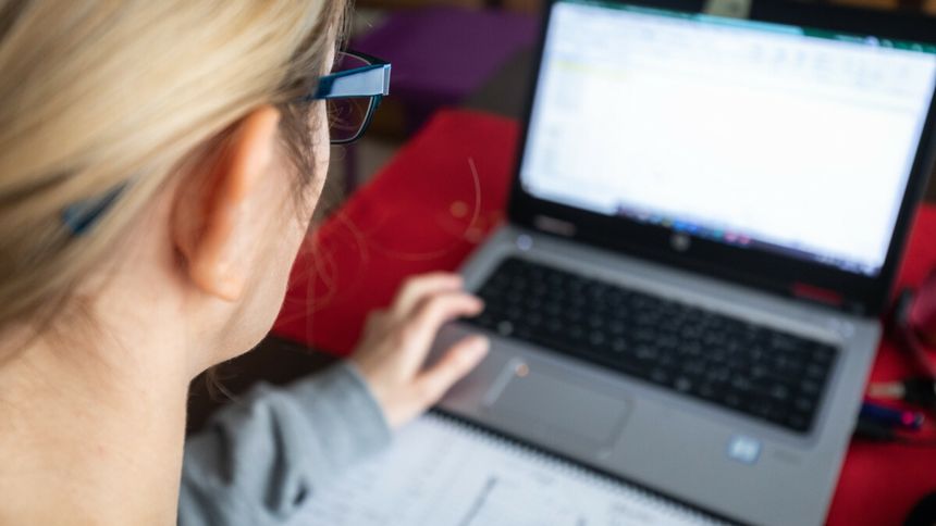 Osoba pracująca przy laptopie, zapisująca notatki na kartce, z widocznym biurkiem.