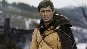 Mężczyzna w średniowiecznym stroju, z zamyśloną miną, w tle rozmyta zima i krajobraz.