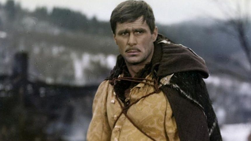 Mężczyzna w średniowiecznym stroju, z zamyśloną miną, w tle rozmyta zima i krajobraz.
