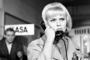 Kobieta w jasnym płaszczu rozmawia przez czarną słuchawkę telefoniczną. 