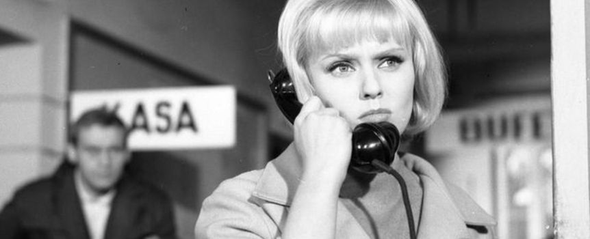 Kobieta w jasnym płaszczu rozmawia przez czarną słuchawkę telefoniczną. 