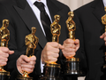 Grupa osób w eleganckich strojach trzyma złote statuetki Oscarów.