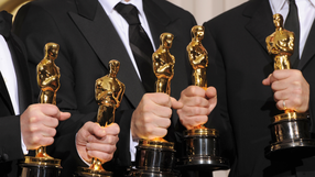 Grupa osób w eleganckich strojach trzyma złote statuetki Oscarów.