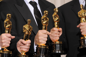 Grupa osób w eleganckich strojach trzyma złote statuetki Oscarów.