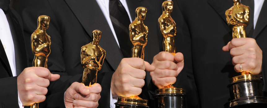 Grupa osób w eleganckich strojach trzyma złote statuetki Oscarów.