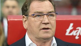 Jan Urban w garniturze siedzi na trybunach, wyrażając emocje podczas wydarzenia.