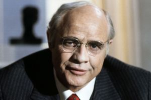 Nie wiem, kto znajduje się na zdjęciu. 

Opis ALT: Mężczyzna w okularach, w eleganckim stroju, z poważnym wyrazem twarzy.