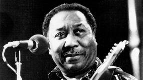 Mężczyzna przy mikrofonie, grający na gitarze, uśmiechnięty.