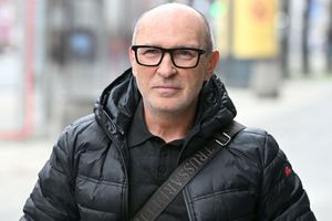 Mężczyzna w czarnej kurtce puchowej, z okularami, uśmiecha się na ulicy.