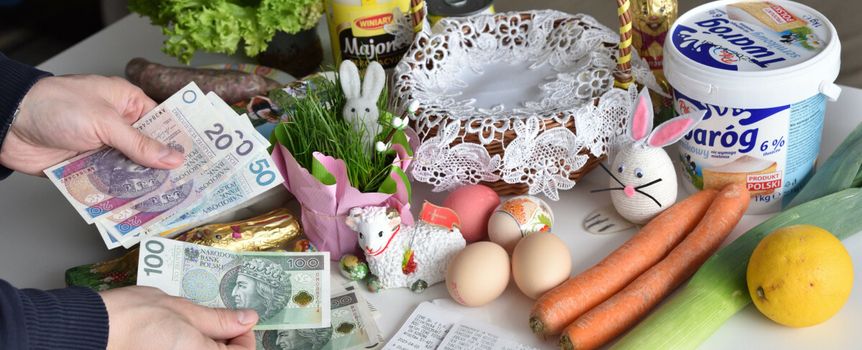 Na stole leżą zakupy wielkanocne: jedzenie, dekoracje oraz pieniądze w rękach.