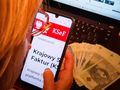Osoba korzystająca z telefonu, na którym wyświetla się strona Krajowego Systemu e-Faktur, obok banknoty.