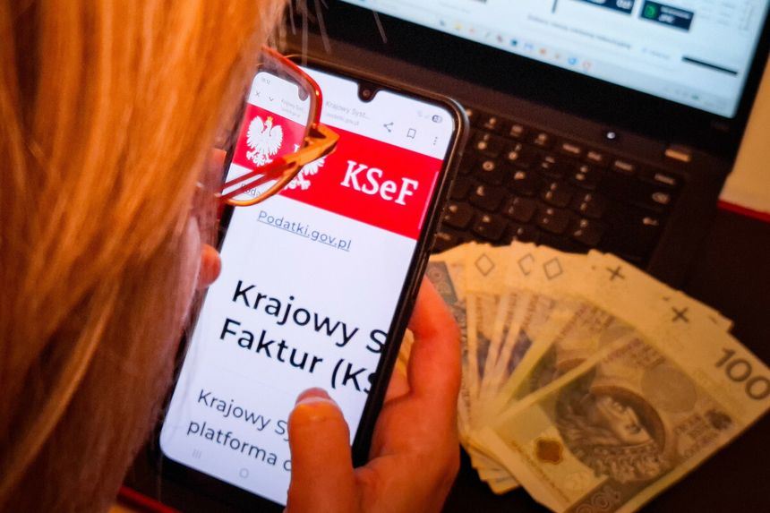 Osoba korzystająca z telefonu, na którym wyświetla się strona Krajowego Systemu e-Faktur, obok banknoty.