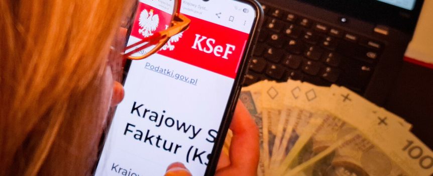 Osoba korzystająca z telefonu, na którym wyświetla się strona Krajowego Systemu e-Faktur, obok banknoty.