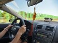 Osoba prowadząca samochód, widok na drogę i zielony płot w tle. Wnętrze pojazdu.