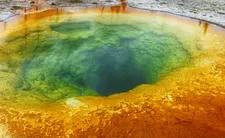 Jasnoniebieska, okrągła dziura w ziemi otoczona kolorowymi minerałami i osadami.