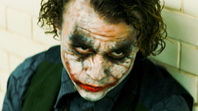 Na zdjęciu Heath Ledger jako Joker - mężczyzna z pobrudzoną twarzą, niebieskimi oczami i kręconymi włosami.
